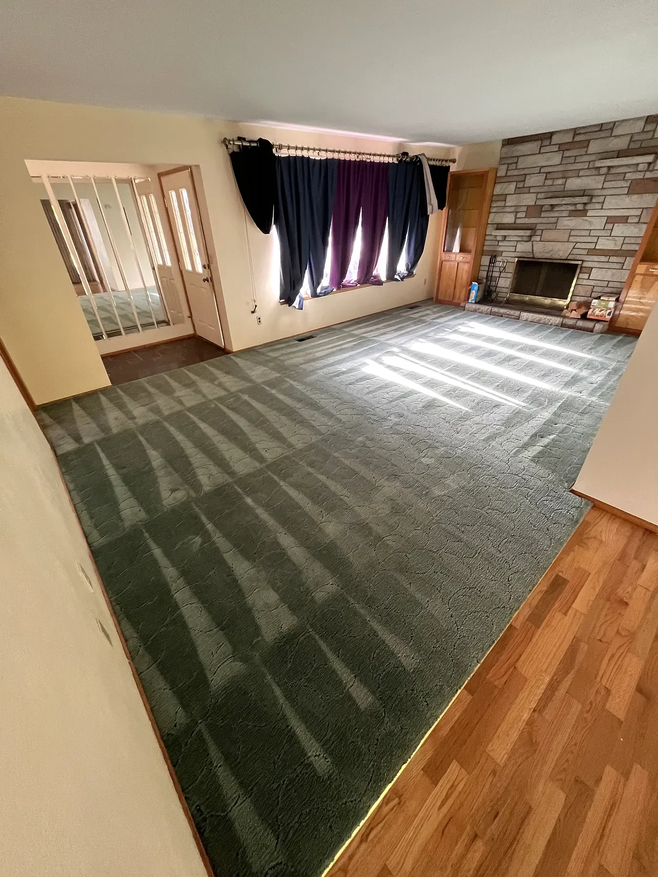 Green living room carpet after cleaning, with a stone fireplace and hardwood floor